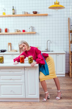 selective focus of beautiful stylish housewife with cans of pickled vegetables on counter in kitchen 