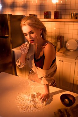 beautiful elegant housewife smoking cigarette while cooking in kitchen with orange light