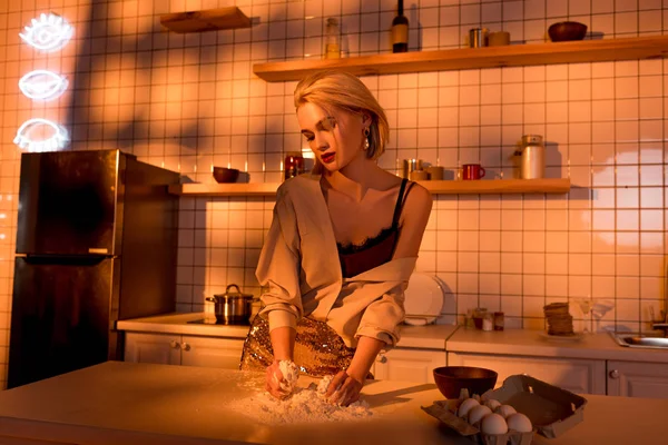 オレンジ色のライトが付いている台所で料理をしてカウンターに小麦粉と美しい主婦 — ストック写真
