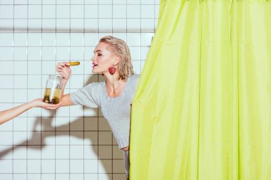 beautiful stylish woman taking pickled cucumber from glass jar in shower