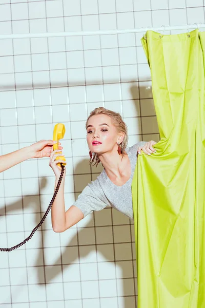 緑のカーテンとシャワーで黄色のレトロな電話の携帯電話を取る美しい女性 — ストック写真
