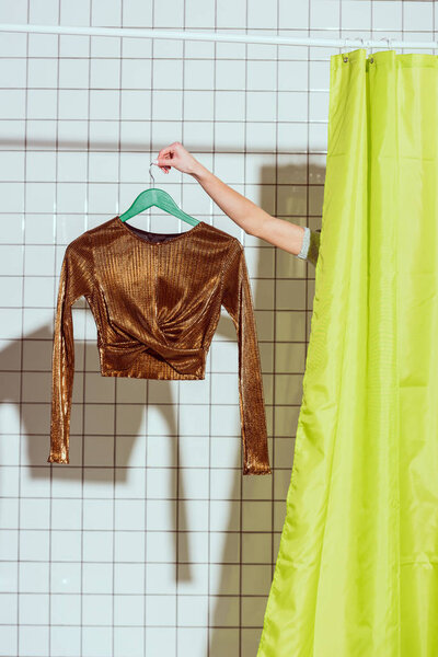 cropped view of woman holding bronze top on hanger in shower with green curtain