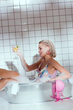 güzel gülümseyen genç kadın kokteyl cam yıkama küvet banyo içinde holding