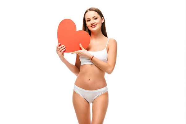 beautiful girl in underwear holding heart shaped card and looking at camera isolated on white
