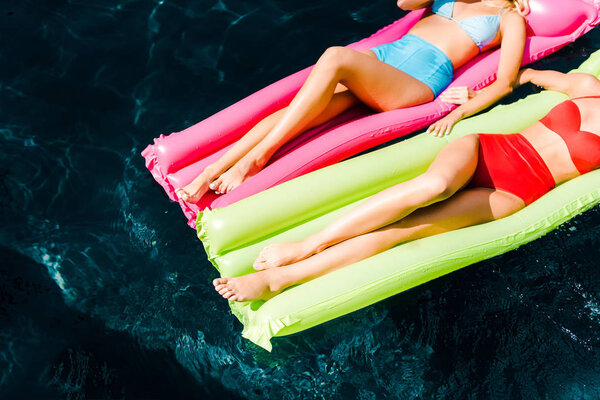 cropped view of girls sunbathing on inflatable mattresses in swimming pool