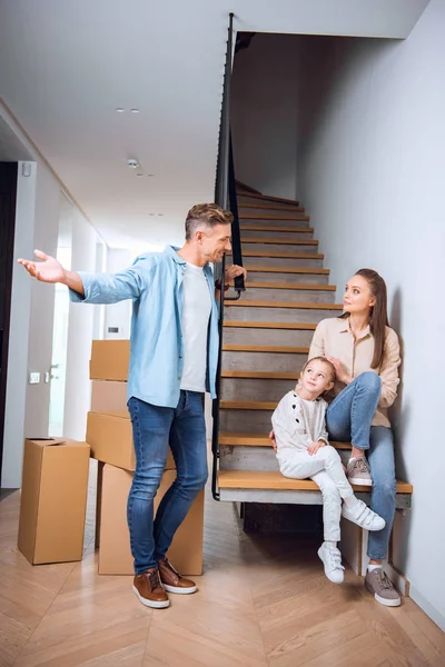 英俊的男人看着可爱的女儿和妻子坐在楼梯上的新家 — 图库照片