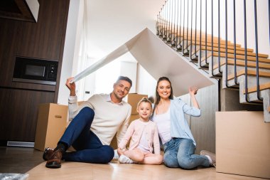 Kağıt çatı altında mutlu aile oturma ve yeni ev gülümseyen 