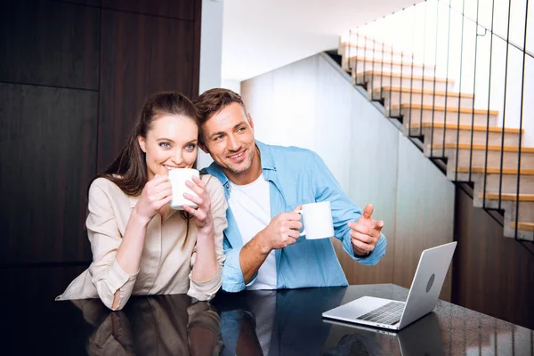 Alegre Hombre Señalando Con Dedo Computadora Portátil Cerca Esposa Bebiendo —  Fotos de Stock