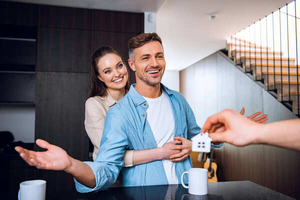 cropped view of man giving house shaped key chain to cheerful couple in new home 