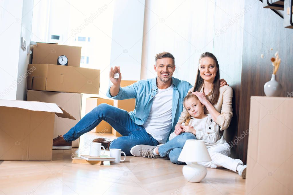 happy man sitting on floor with house shaped key chain near attractive wife and daughter 