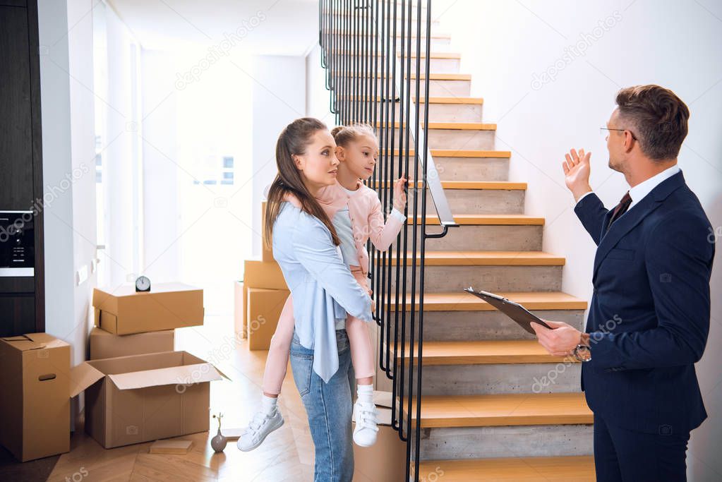 handsome broker showing stairs to attractive woman holding in arms cute daughter 
