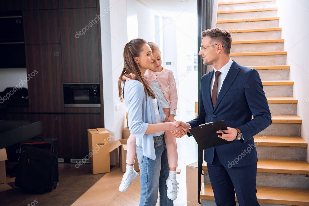 attractive woman shaking hands with broker while holding in arms daughter 