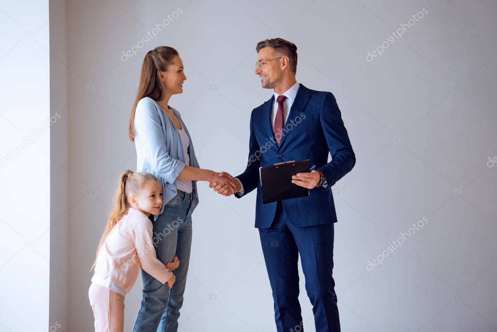 handsome broker shaking hands with attractive woman standing with cute daughter