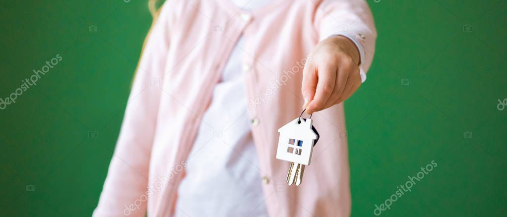 cropped view of kid holding house shaped key chain isolated on green