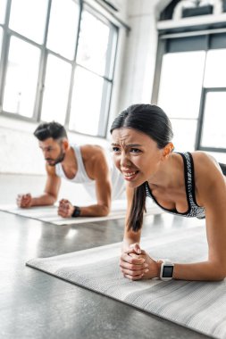 Genç kadın ve erkek spor salonunda yoga paspaslar üzerinde tahta egzersiz yaparak yoğunlaştı 