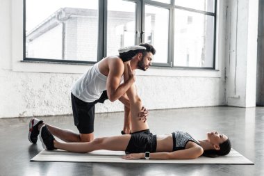 kaslı adam genç sporcumuz spor salonunda yoga mat bacak Germe yardım yan görünüm