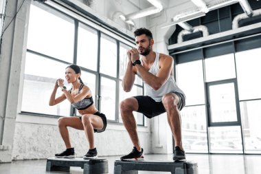 low angle view of concentrated sportive young couple in sportswear training with step platforms in gym  clipart