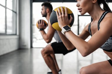 cropped shot of sporty young couple holding medicine balls and training together in gym