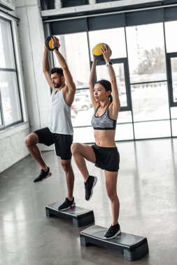 Tam boy görünüm atletik genç çiftin sağlık toplarıyla tutarak ve adım platformlar spor salonunda egzersiz