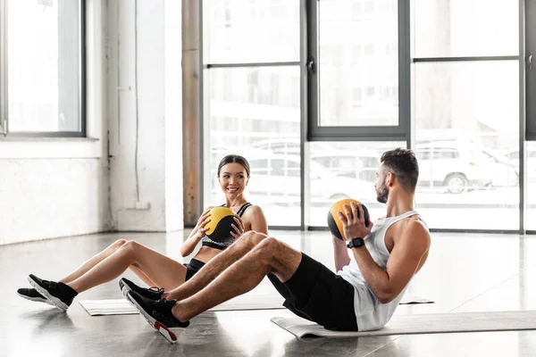 年轻夫妇拿着药球 微笑着在健身房的瑜伽垫训练 — 图库照片