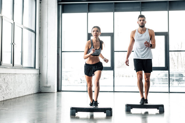 мускулистый молодой человек и красивая спортивная девушка вместе тренируются на ступенчатых площадках в спортзале
 