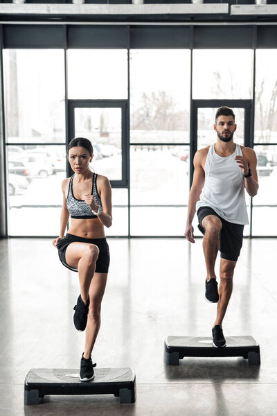 full length view of athletic young couple training on step platforms in gym 