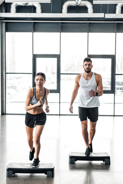 full length view of sporty young couple exercising on step platforms in gym 