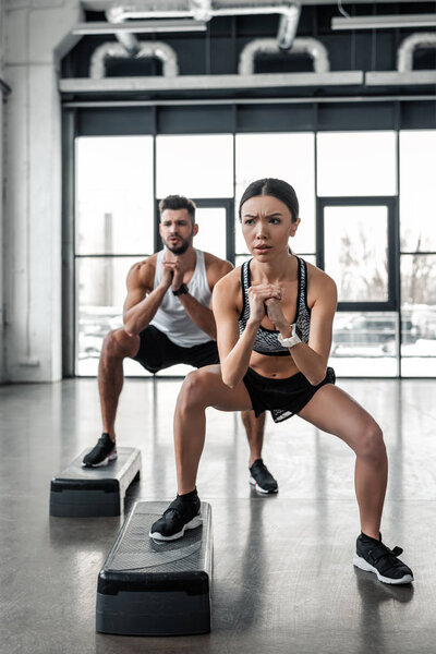 full length view of concentrated young couple exercising with step platforms in gym