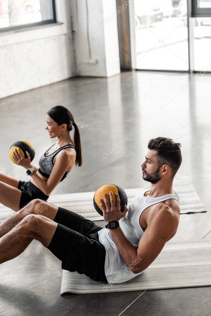 high angle view of athletic young couple holding medicine balls and doing abs exercise on yoga mats