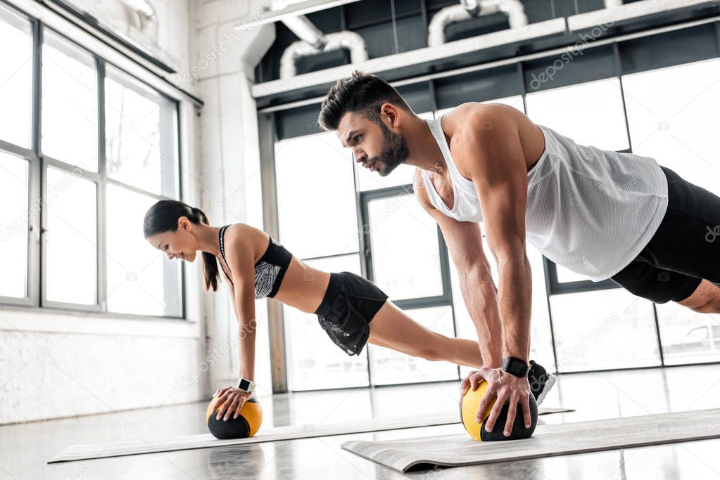 side view of athletic young couple in sportswear exercising with medicine balls on yoga mats in gym