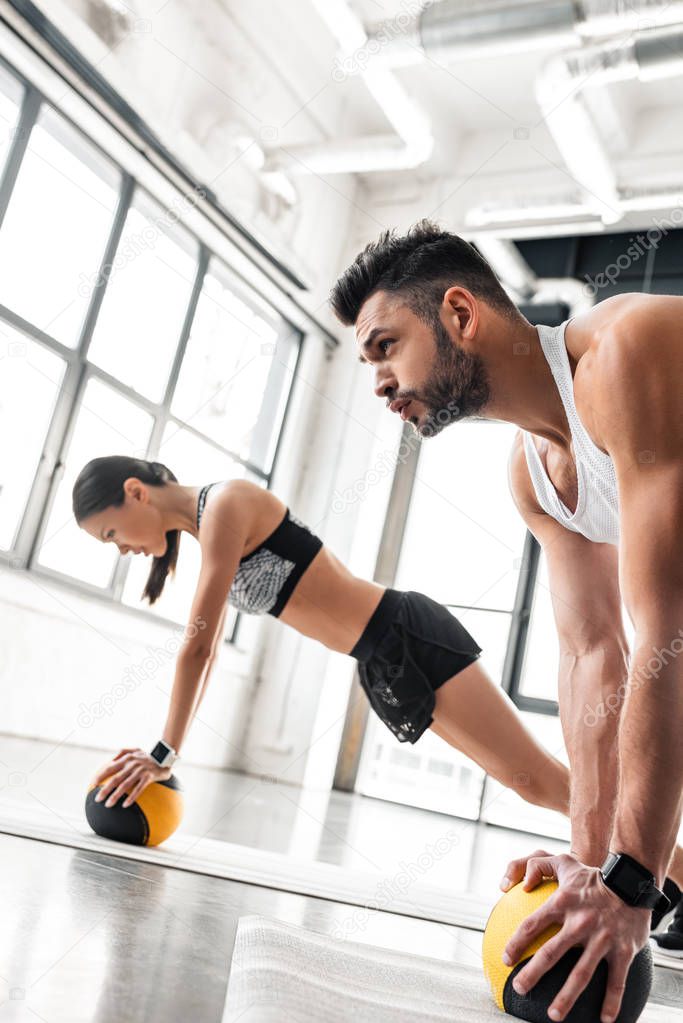 muscular young man and sporty girl exercising with medicine balls on yoga mats