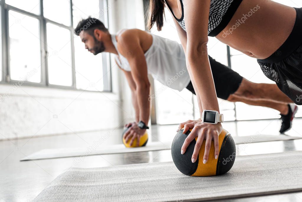cropped shot of young sportive couple exercising with medicine balls on yoga mats