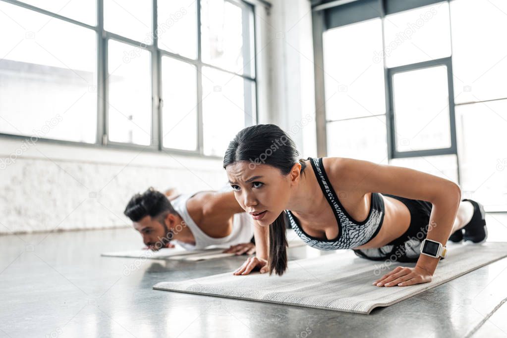 athletic concentrated young woman and man doing push ups on yoga mats in gym 
