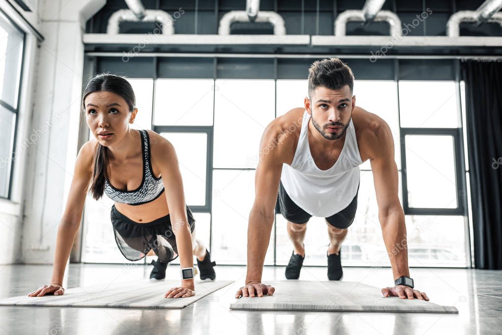 concentrated sporty young couple doing push ups on yoga mats in gym