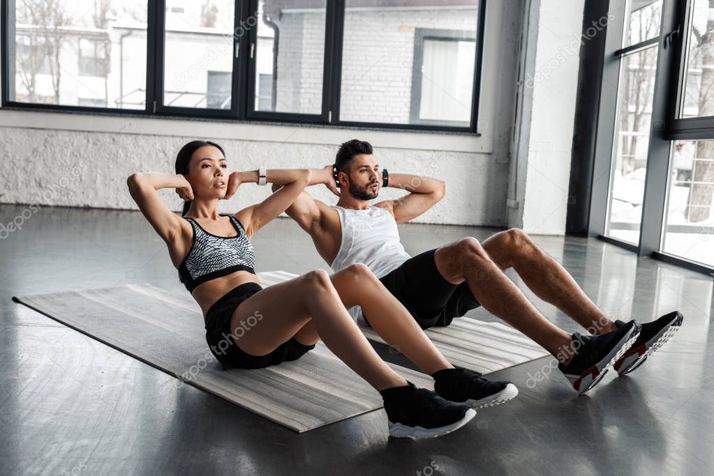 athletic young couple doing abs exercise on yoga mats in gym