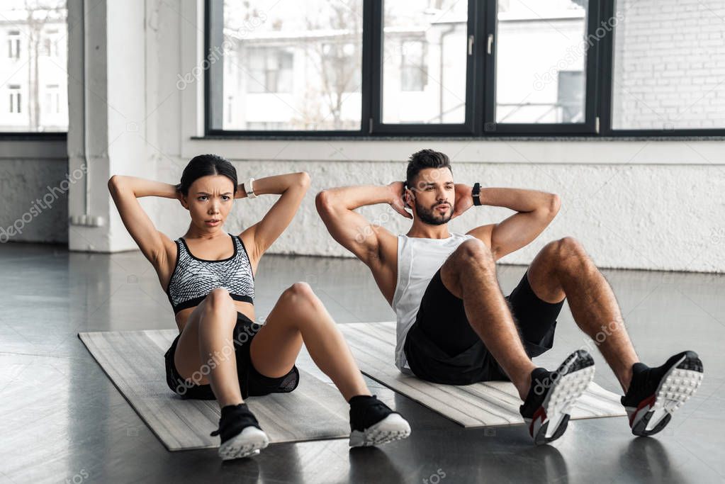 sporty young couple doing abs exercise on yoga mats in gym