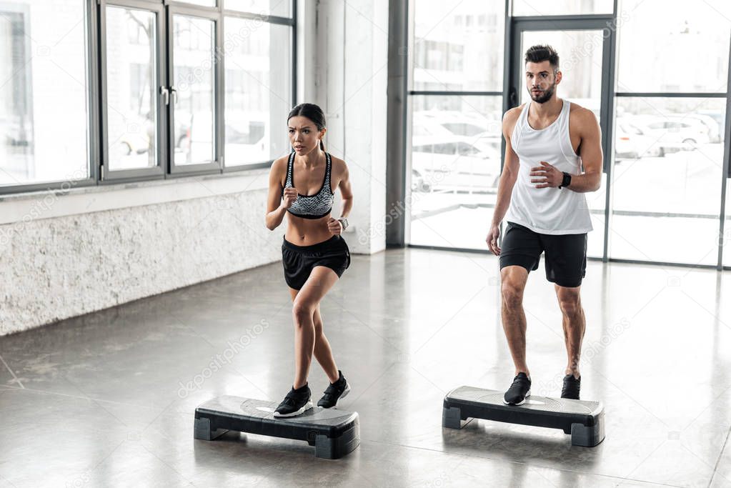 muscular young man and beautiful sporty girl exercising together on step platforms in gym 