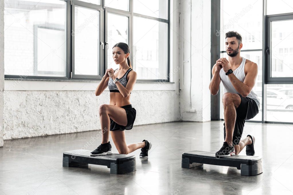 muscular young man and beautiful sporty girl training on step platforms in gym