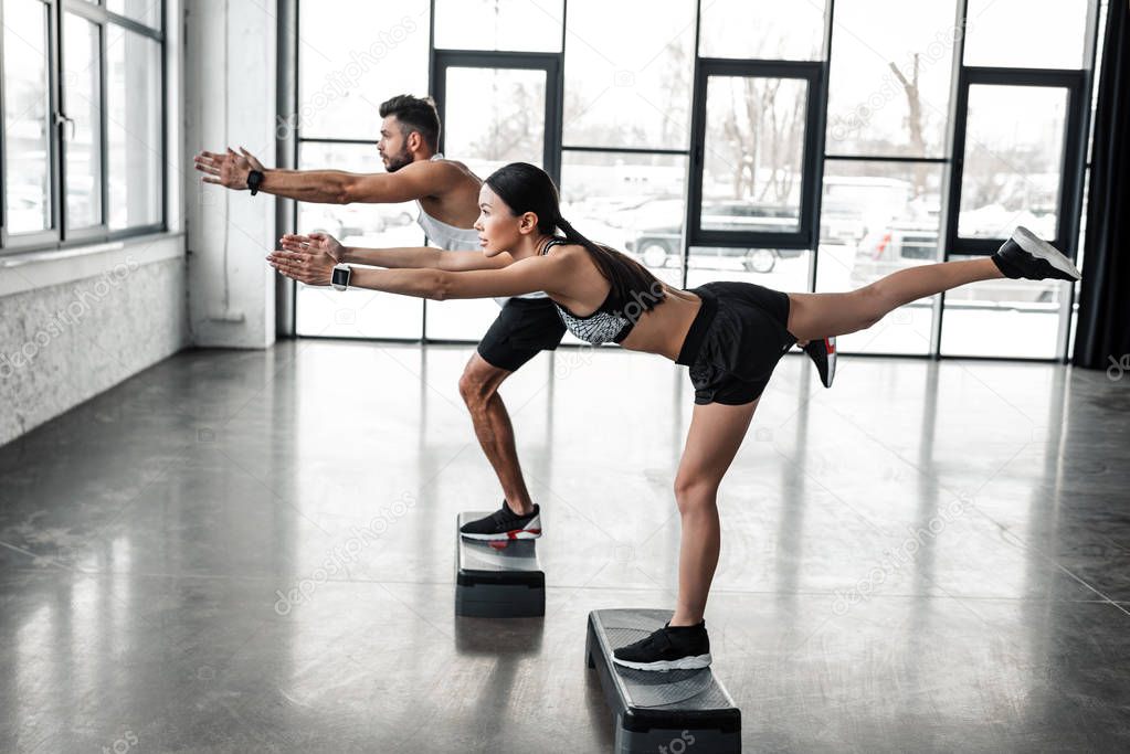 side view of athletic young man and woman in sportswear exercising with step platforms in gym