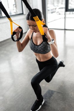 high angle view of focused young sportswoman exercising with suspension straps in gym 