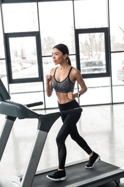 beautiful young sportswoman running on treadmill in gym  clipart