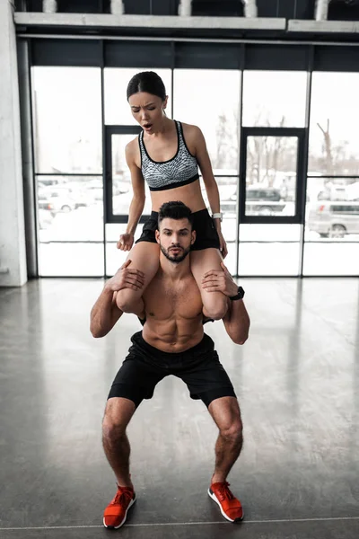 Jovem Sem Camisa Muscular Agachando Com Menina Esportiva Nos Ombros — Fotografia de Stock