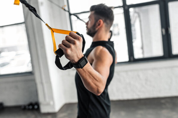 side view of muscular young man in sportswear training with resistance bands in gym