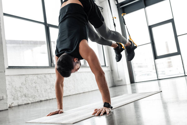 athletic young man performing handstand on yoga mat and training with resistance bands in gym