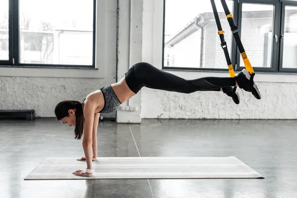 在健身房的瑜伽垫上 运动的年轻女子用吊带锻炼的侧视图 — 图库照片