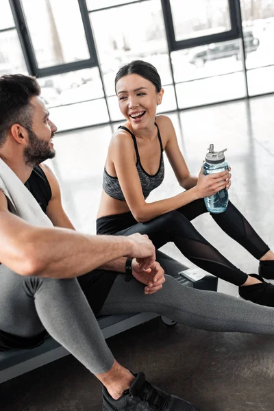 幸福的年轻夫妇用毛巾和一瓶水坐在一起在健身房的跑步机上 — 图库照片