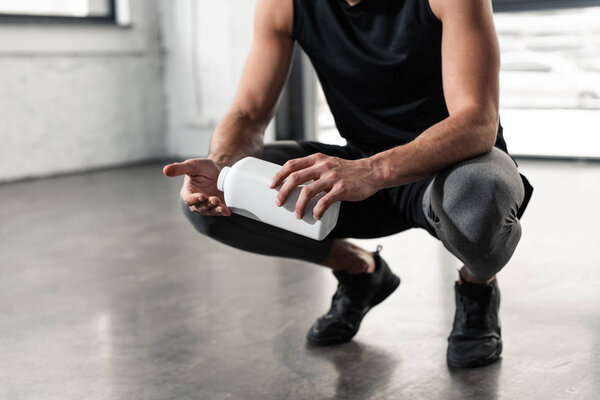 cropped shot of sportsman holding plastic container and applying talcum powder on hands in gym