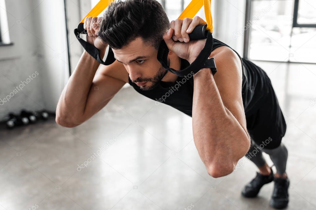 close-up view of concentrated sporty man hanging on fitness straps and looking away in gym