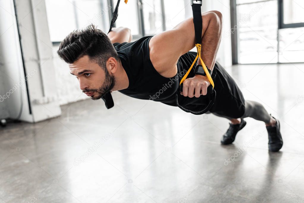 athletic handsome young sportsman exercising with resistance bands in gym