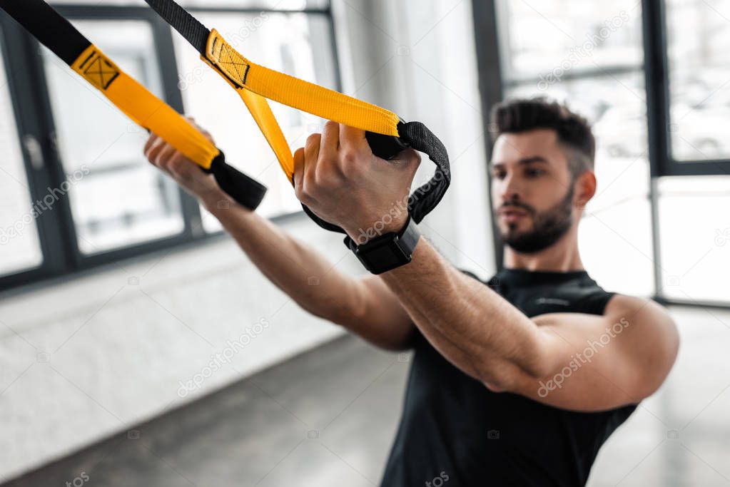 close-up view of athletic muscular young man in sportswear training with resistance bands in gym